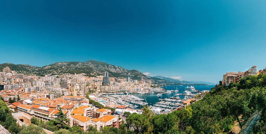 Monaco, Monte Carlo cityscape. Real estate architecture on mountain hill background. Many high-rise buildings in downtown area. Yachts moored at town quay In Sunny Summer Day